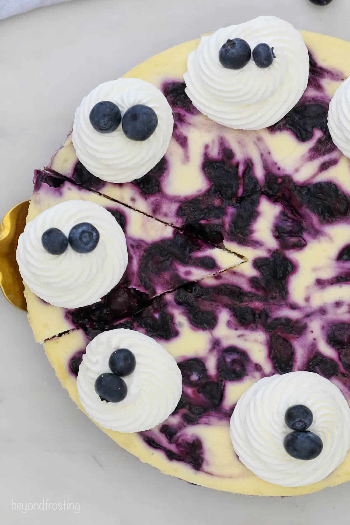 Overhead view of a the top of a cheesecake with blueberries and whipped cream