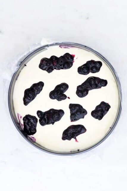 overhead view of a cheesecake batter in a pan with drops of blueberry sauce