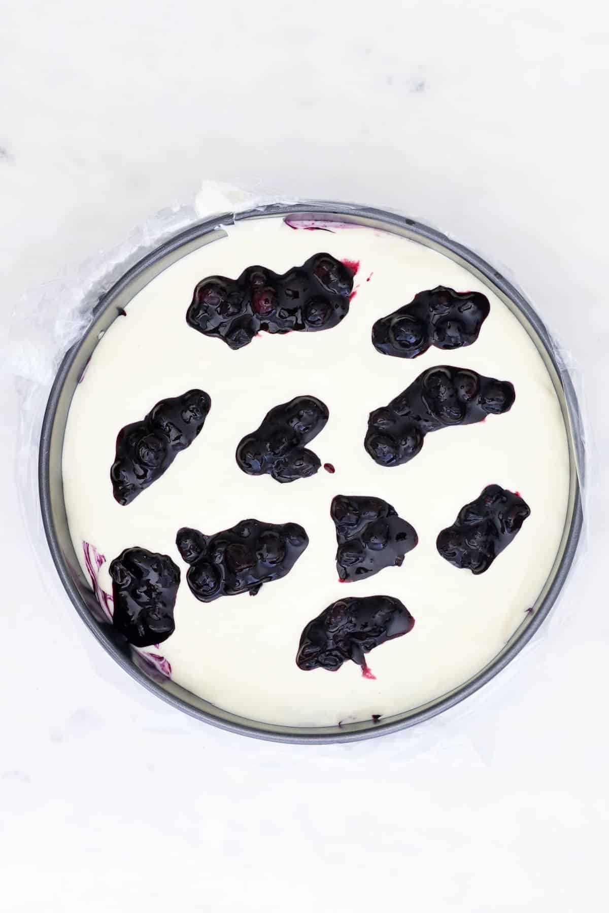 Overhead view of dollops of blueberry sauce added to cheesecake batter inside a springform pan.