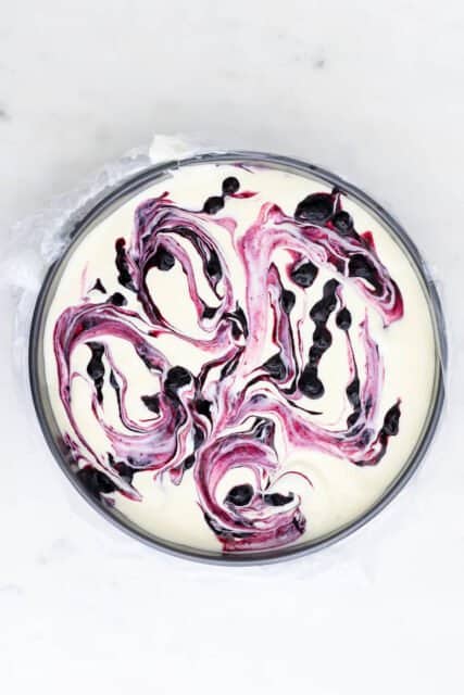 overhead view of an unbaked cheesecake swirled with blueberry sauce