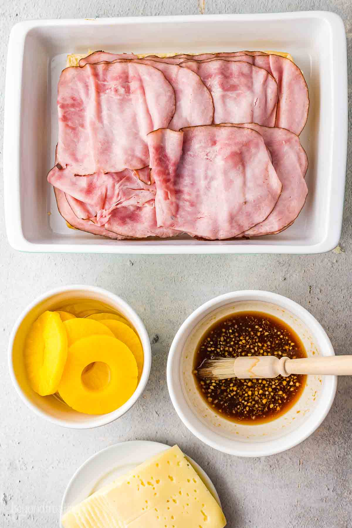 Ham slices over the rolls with a bowl of pineapple rings, the marinade, and cheese on the side.