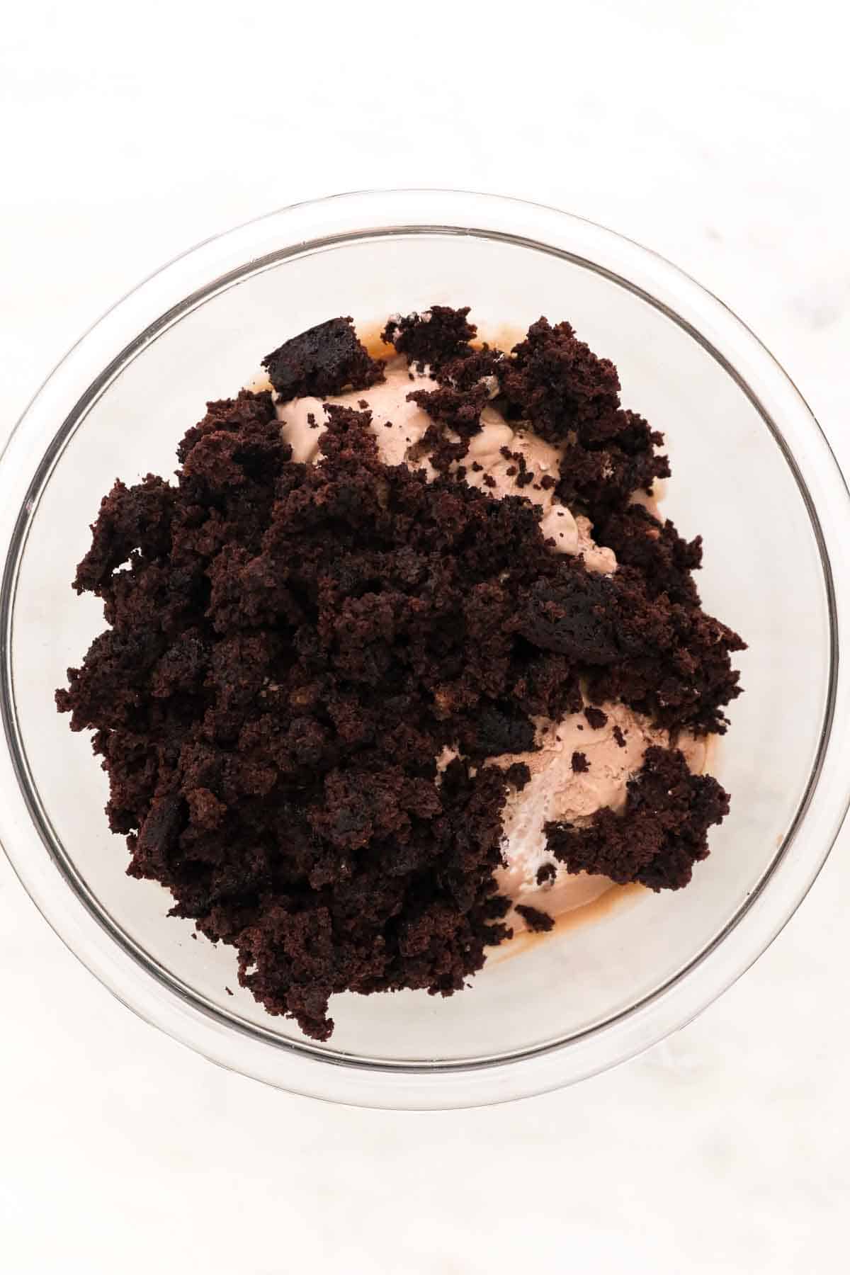 a glass mixing bowl with softened ice cream and chocolate cake crumbs
