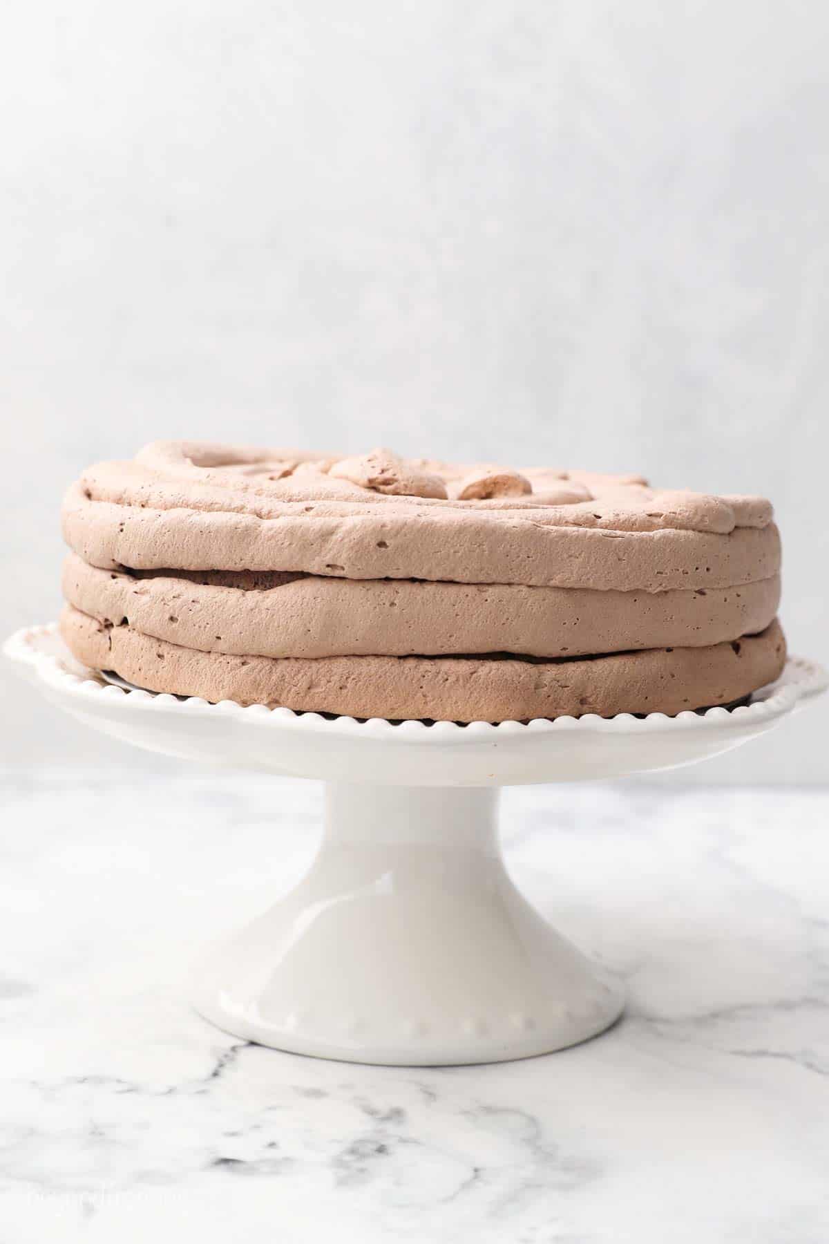 a white cake stand with a cake being frosted with chocolate whipped cream