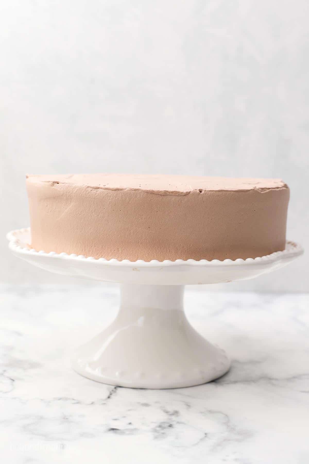 a white cake stand with a small layer cake frosted with chocolate whipped cream
