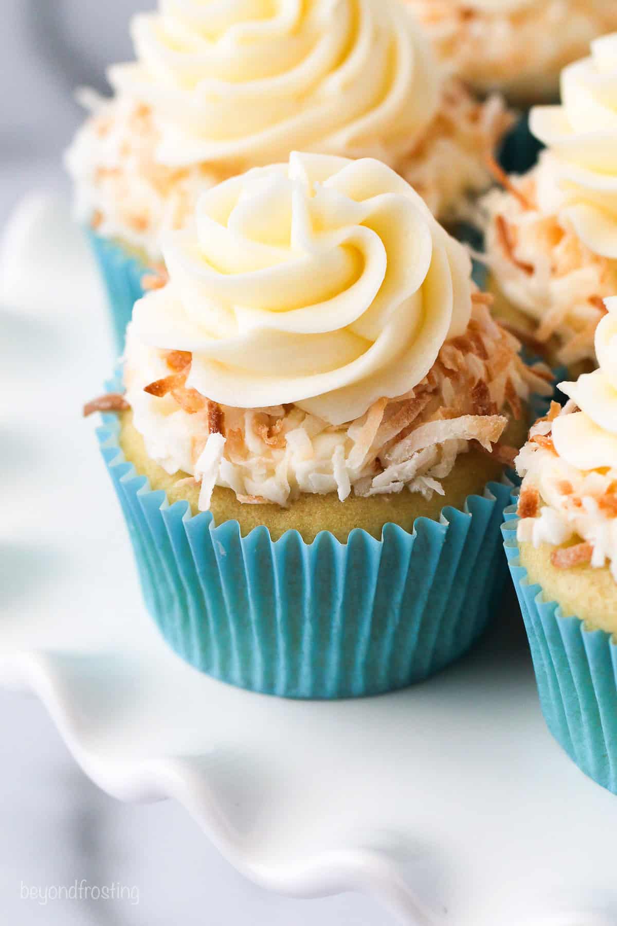 Coconut cupcakes in blue cupcake liners topped with swirls of coconut frosting and toasted coconut.