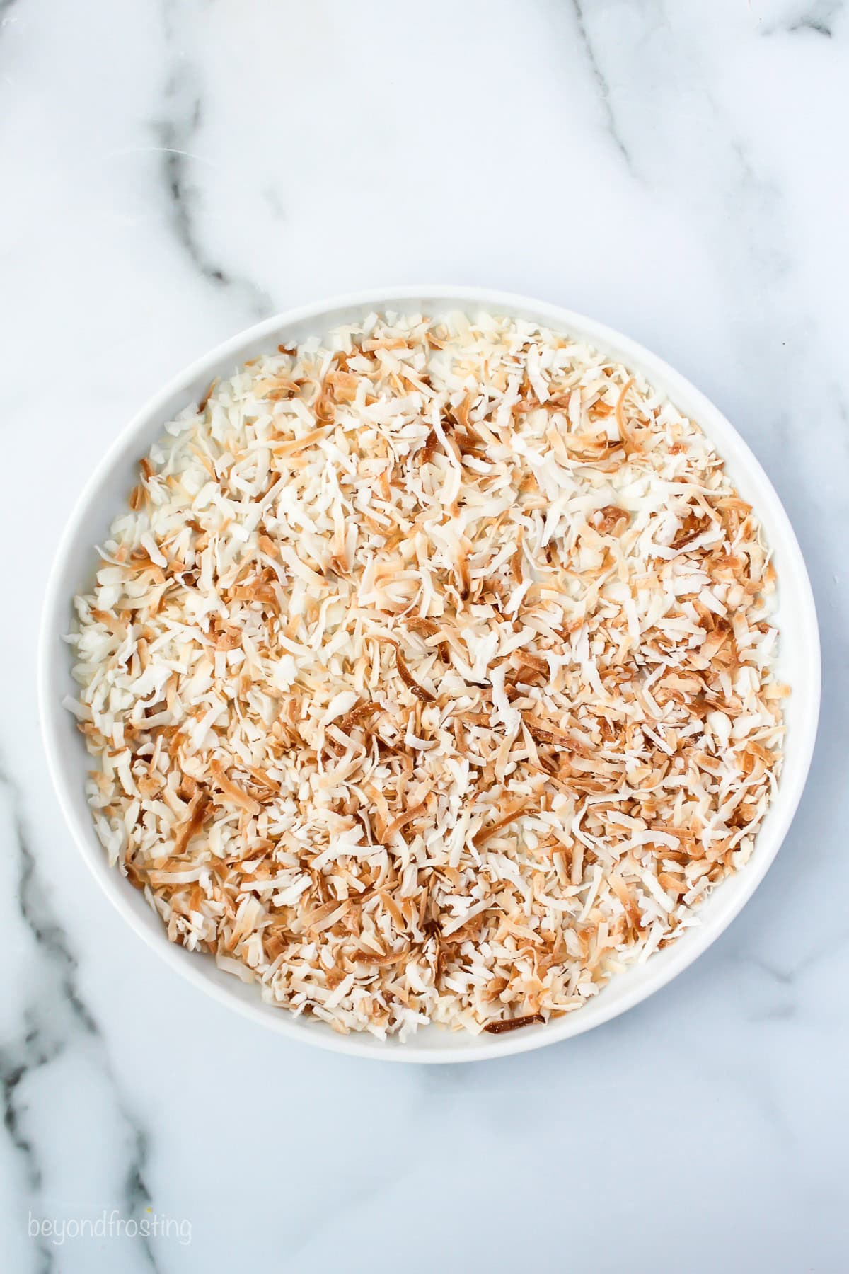 Overhead view of toasted coconut in a round shallow dish.