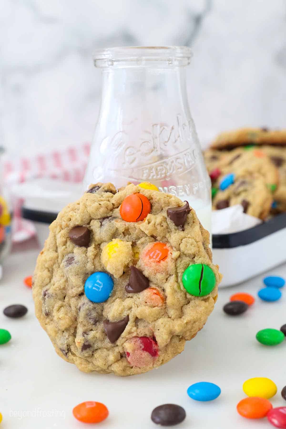 A Monster Cookie resting against a glass of milk.