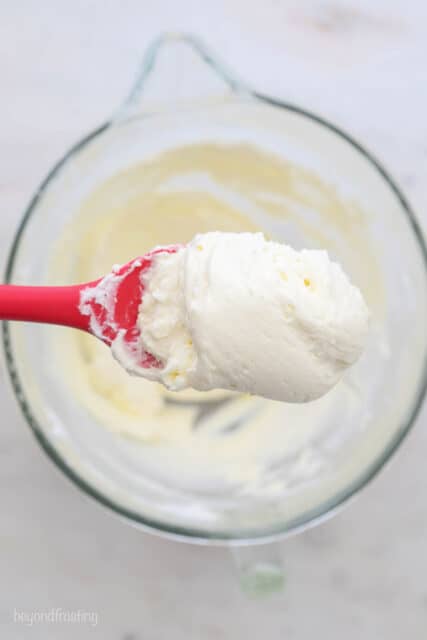 A Bird's Eye View of a glass mixing bowl, a red spatula and a close up of some whipped cream cheese