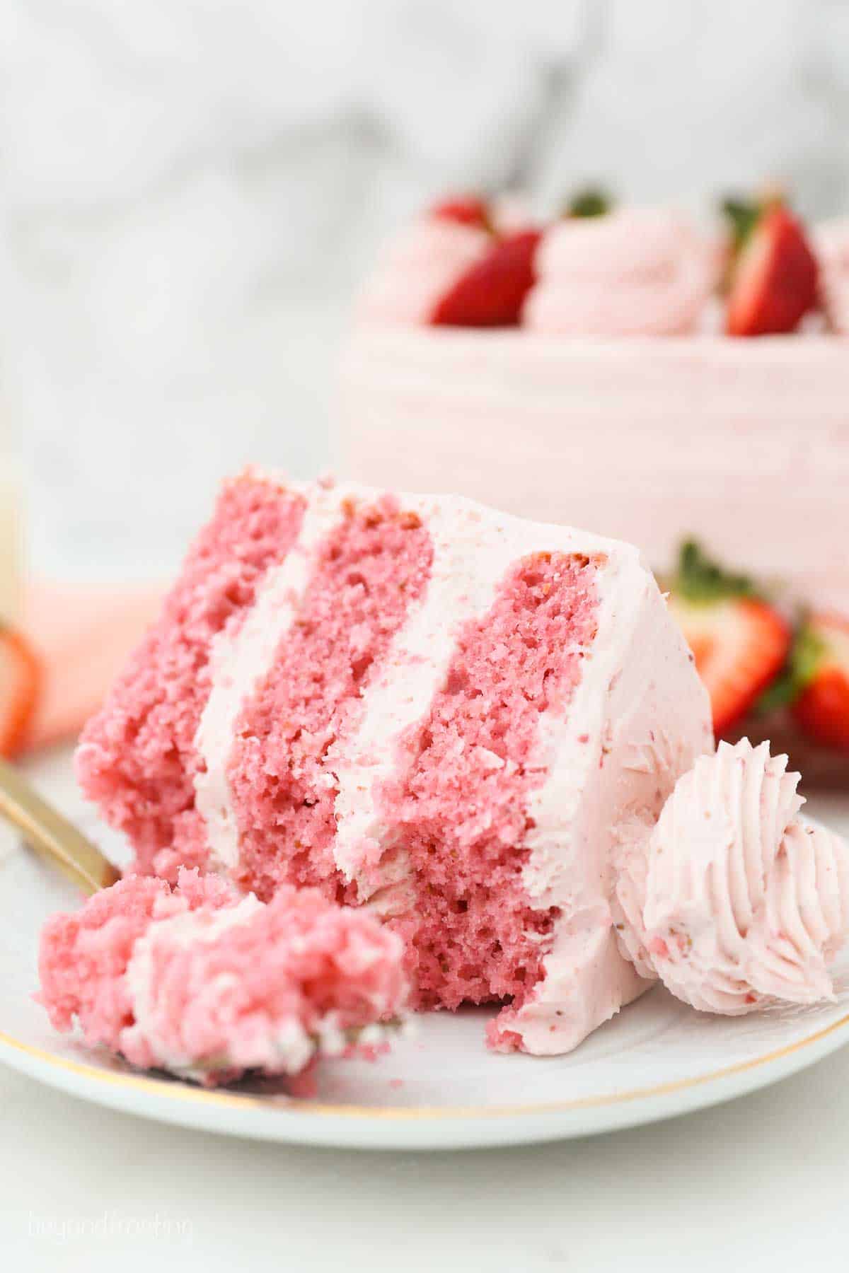 A slice of Strawberry Cake with Strawberry Frosting on its side with a forkful in front.