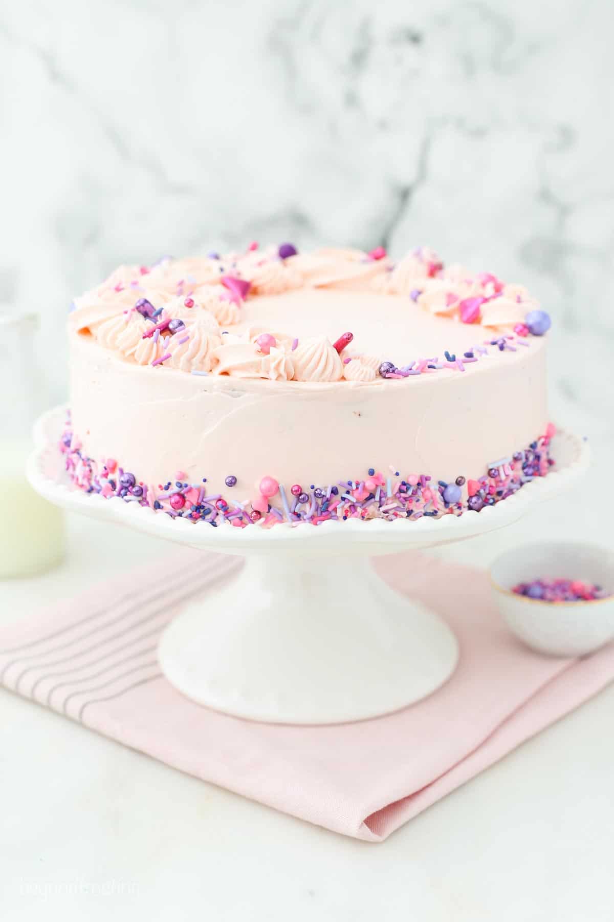A fully decorated White Cake covered in Swiss Meringue Buttercream and sprinkles on a cake platter.