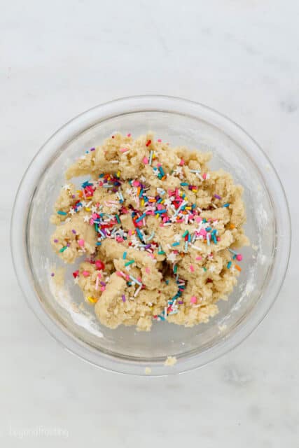 overhead view of a glass mixing bowl with cookie dough and sprinkles