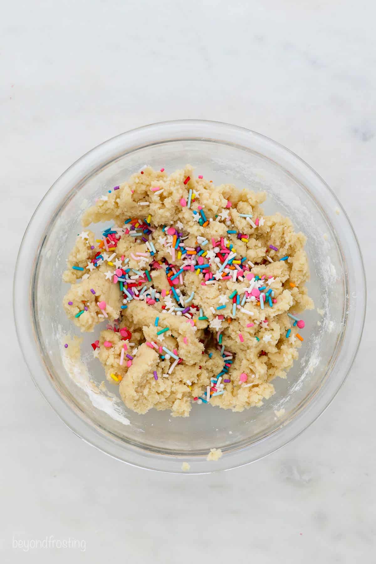 This easy edible sugar cookie dough is egg-free and made with heat-treated flour. It's safe to eat and just as good as the baked version! Overhead view of a glass mixing bowl with sugar cookie dough and sprinkles.