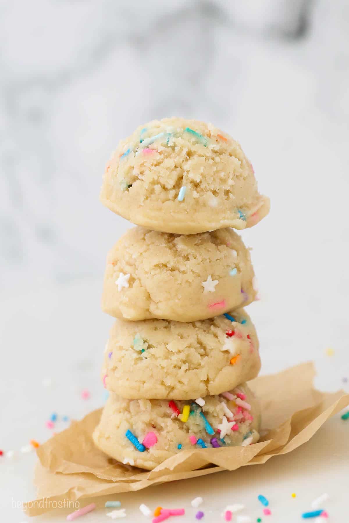 A stack of 4 scoops of cookie dough with sprinkles on brown parchment paper