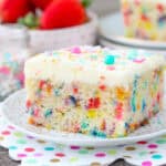 A slice of funfetti cake with buttercream and sprinkles on a gold polka dot plate