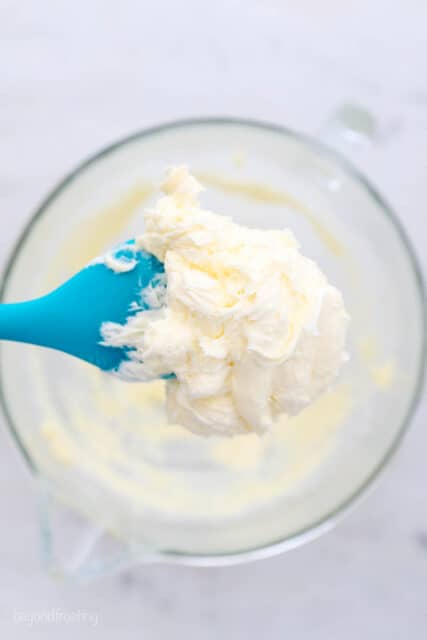 a teal spatula with whipped butter over a mixing bowl