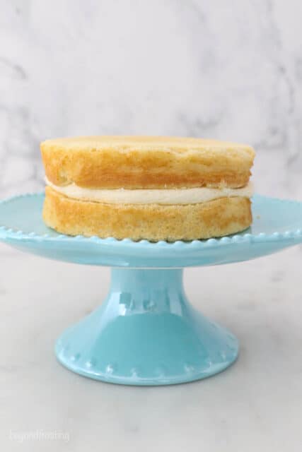 a small teal cake stand with two layers of vanilla cake with frosting in between