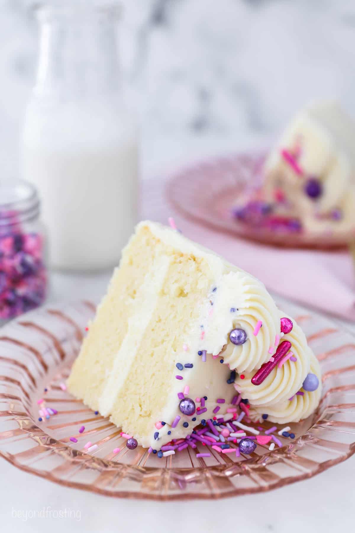 a small slice of vanilla cake with pink and purple sprinkles on a pink glass plate