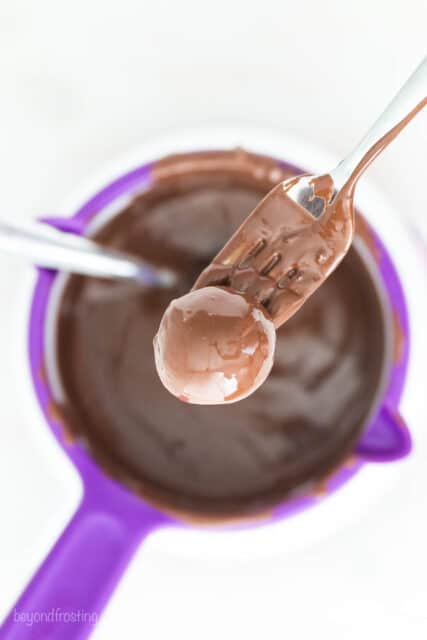 Using a fork to remove the chocolate-covered truffles from the chocolate.