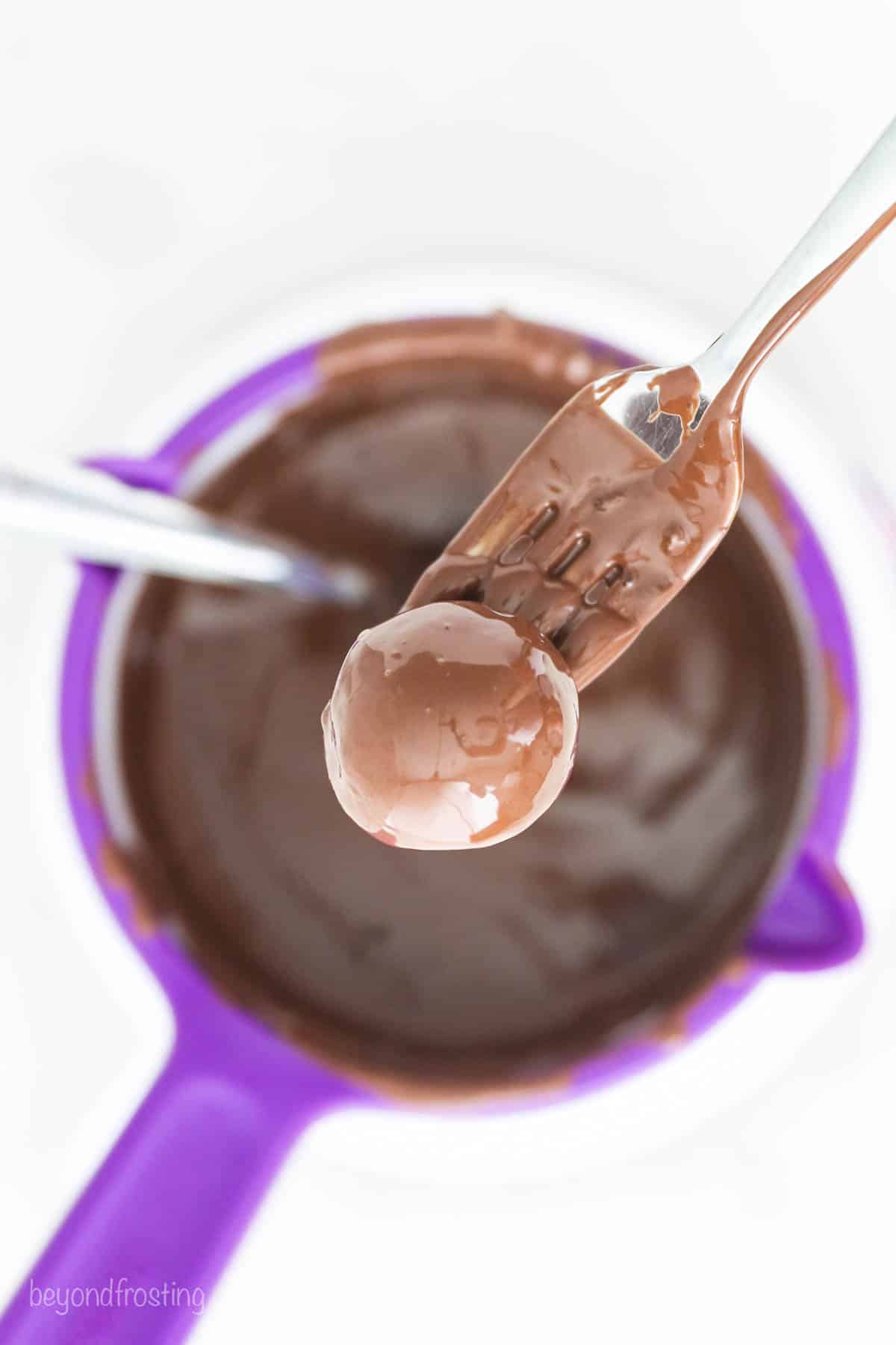Oreo truffles come together fast, no baking required! With only 3 ingredients, these bite-sized Oreo balls make easy edible holiday gifts. Using a fork to remove the chocolate-covered truffles from the chocolate.