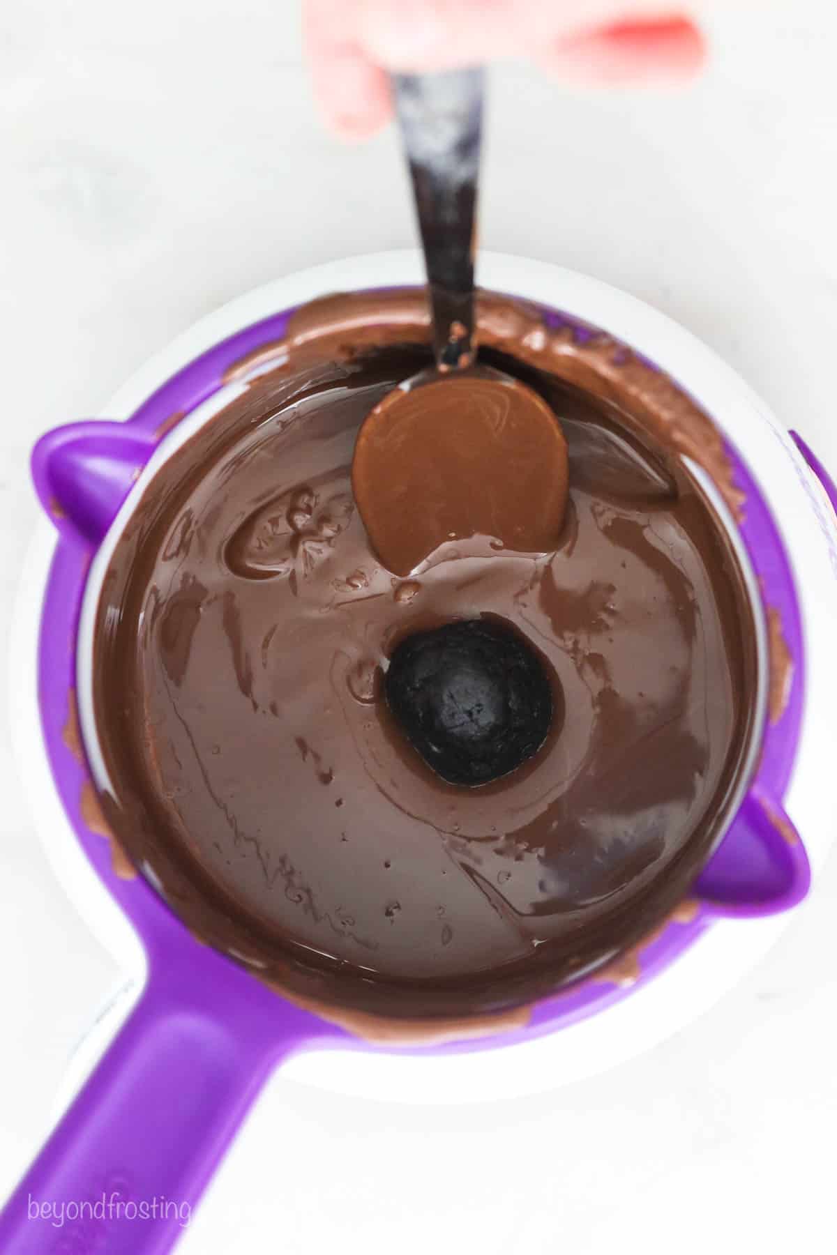 Oreo truffles come together fast, no baking required! With only 3 ingredients, these bite-sized Oreo balls make easy edible holiday gifts. Using a spoon to dip the truffles into the melted chocolate.