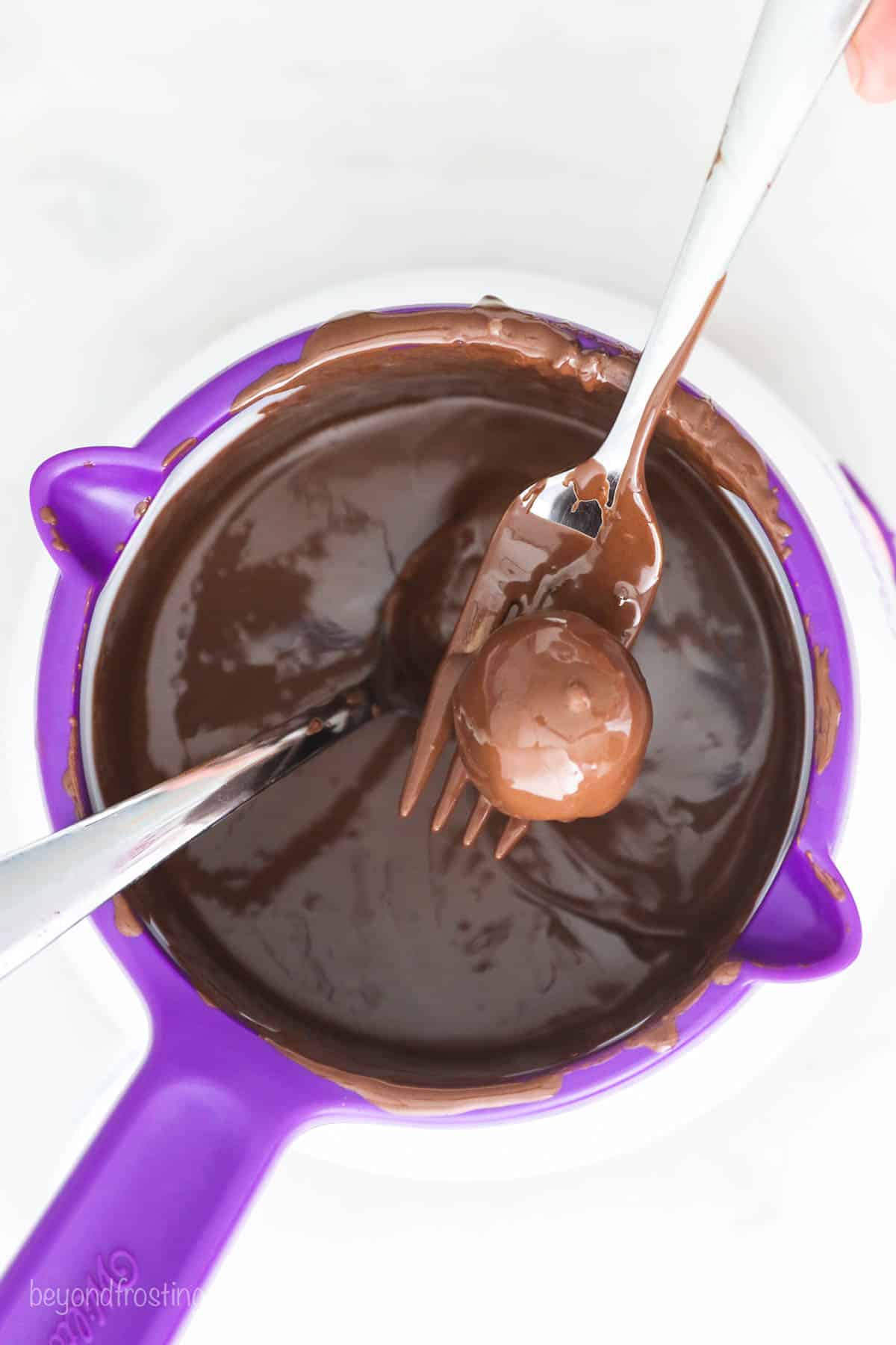 Oreo truffles come together fast, no baking required! With only 3 ingredients, these bite-sized Oreo balls make easy edible holiday gifts. Using a fork to remove the chocolate-covered truffles from the chocolate.