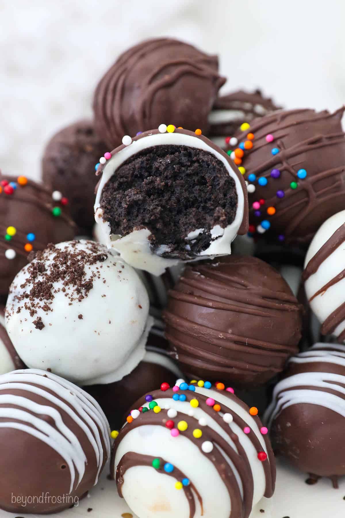 A pile of finished Oreo Truffles on a plate with one cut in half, showing the fudgy Oreo inside.