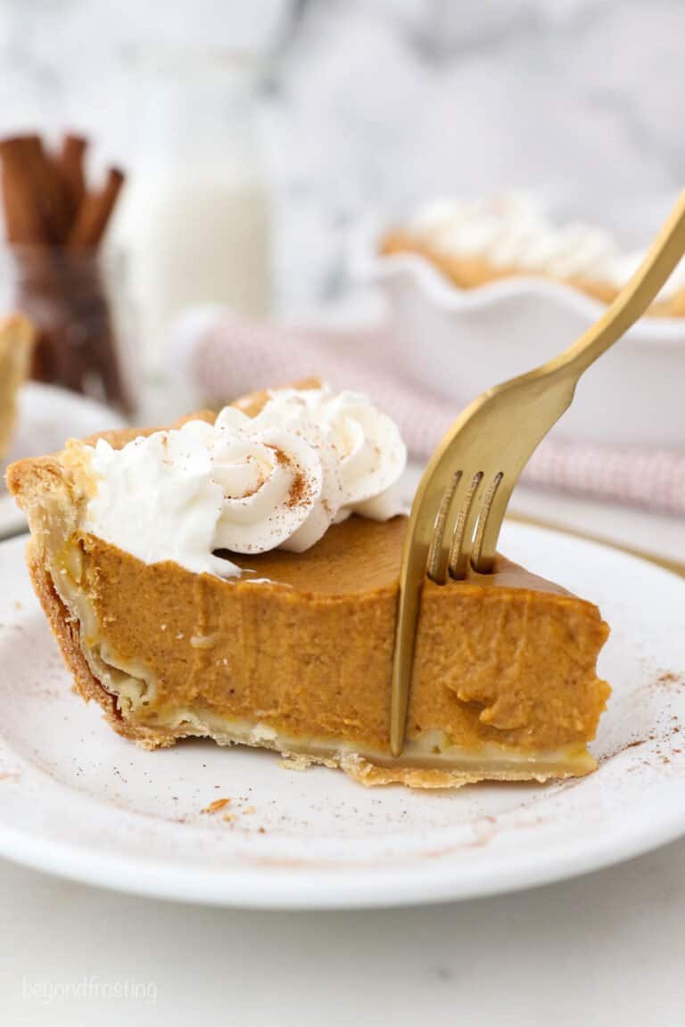 A fork cutting into a slice of Pumpkin Pie with Homemade Whipped Cream.