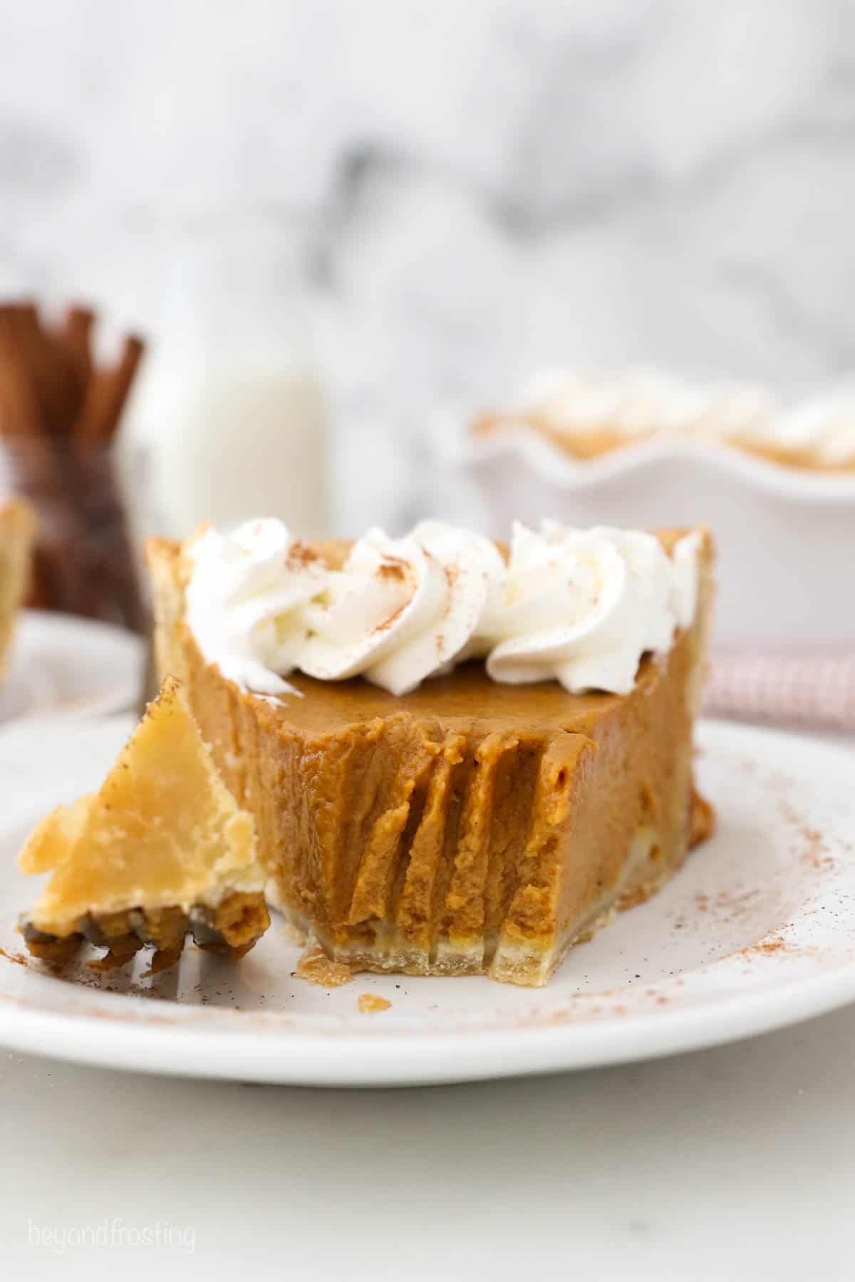 A slice of Pumpkin Pie with Homemade Whipped Cream with a piece taken out from a fork.