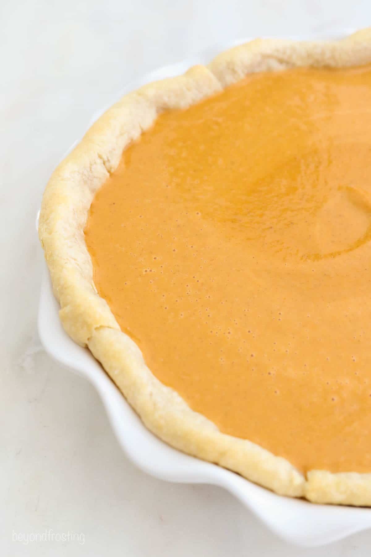 The unbaked pie with the partially baked crust and raw pumpkin filling.