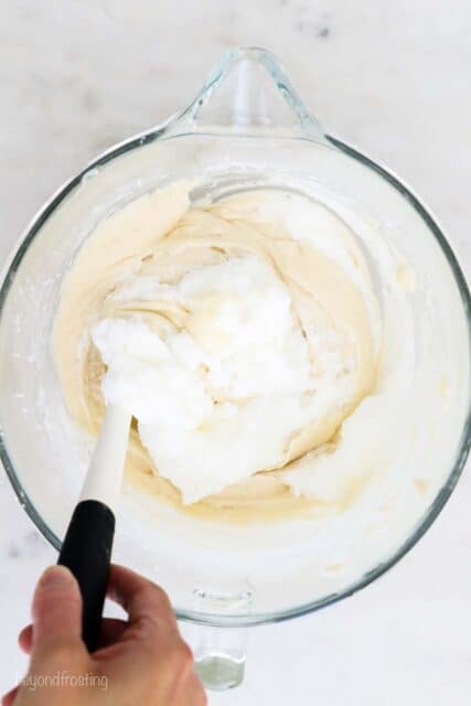 a glass mixing bowl with a white spatula folding egg whites into a cake batter