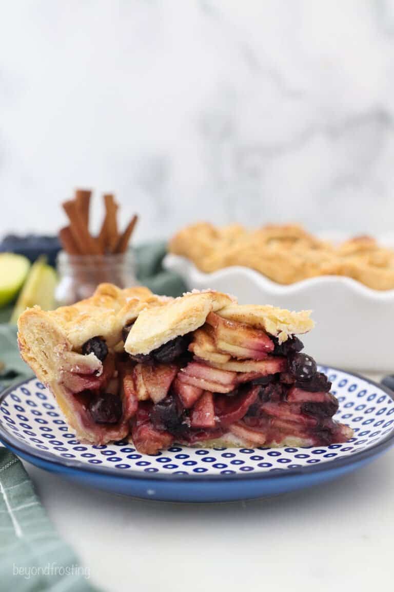A side view of slice of apple and blueberry filled pie on a blue polka dot plate