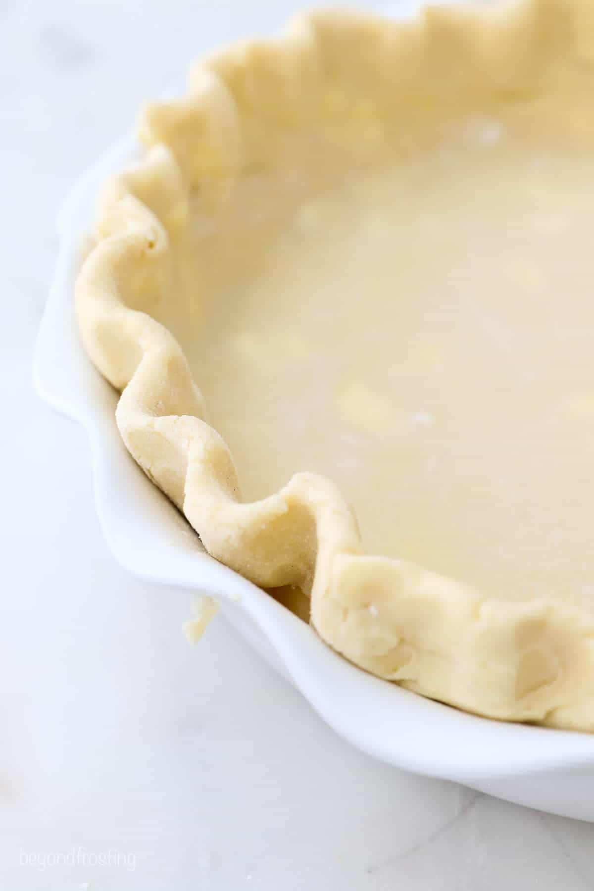 A close-up shot of the crimped edges of a homemade gluten free pie crust in a white pie dish