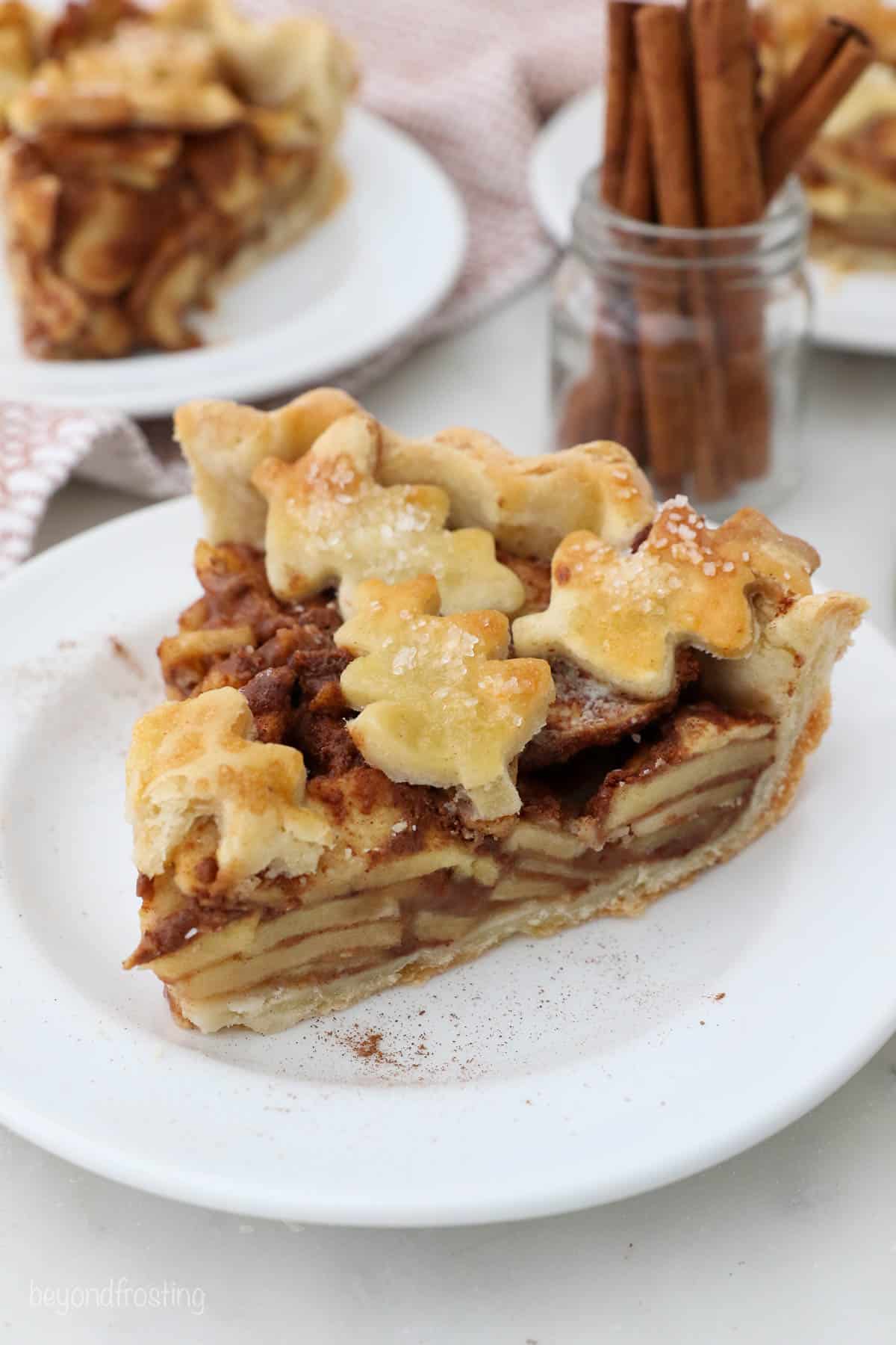 A shot of a slice of apple pie on a white plate, the pie is decorated with leaf shaped pie dough cut outs