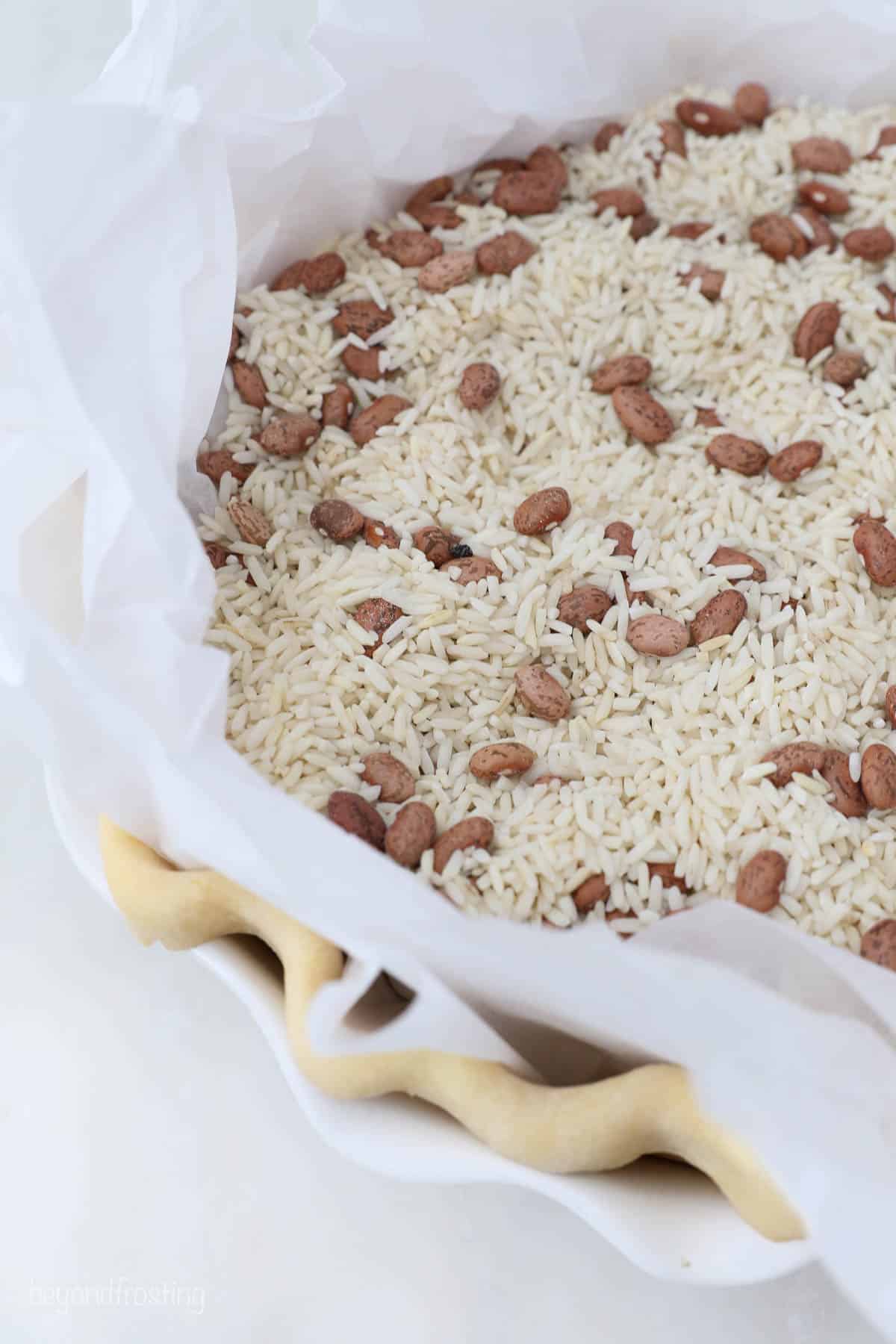 A pie crust lined with two sheets of parchment paper and filled with dry rice and beans
