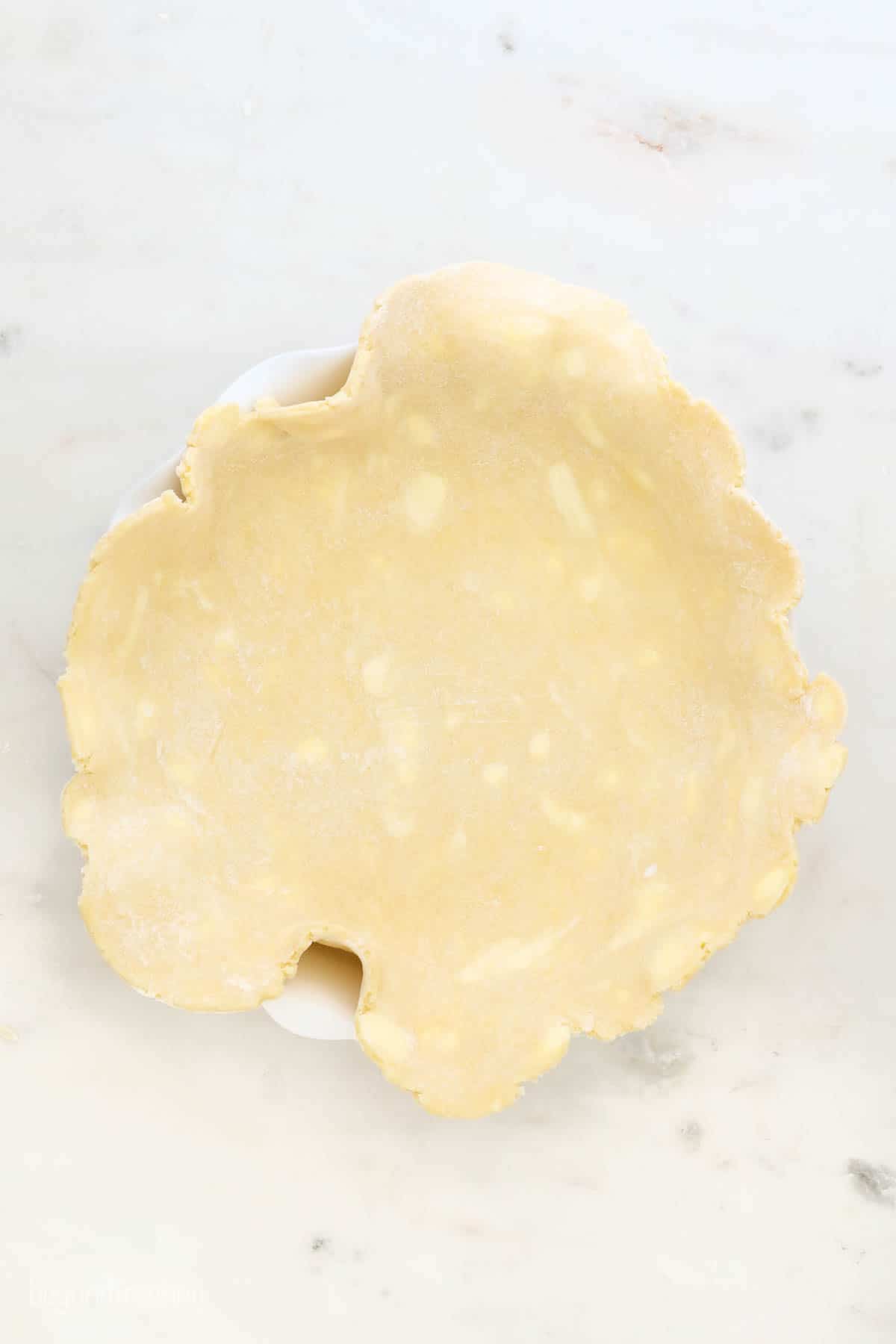 An 11-inch slab of pie crust dough draped over a white pie plate