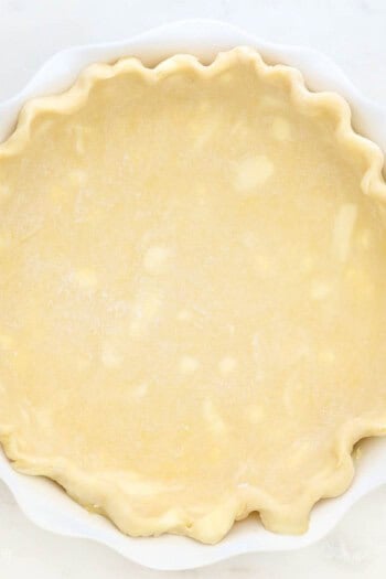 An unbaked pie crust with crimped edges in a white pie plate