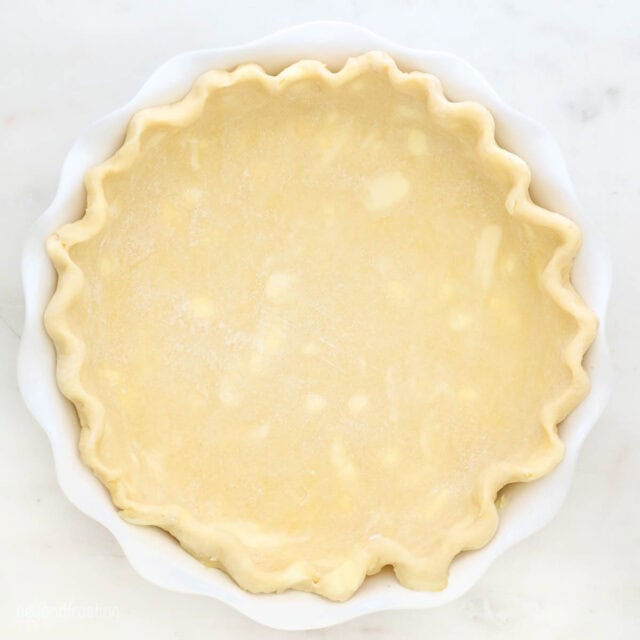 An unbaked pie crust with crimped edges in a white pie plate