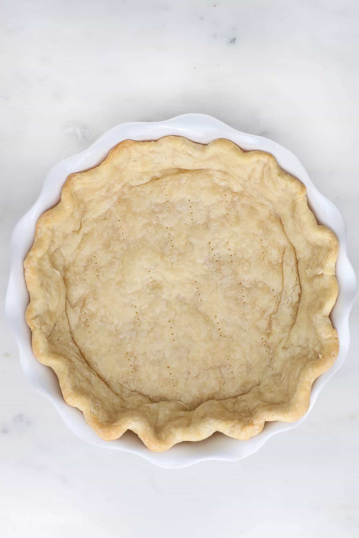 A partially baked pie crust with pinched edges inside of a white pie plate