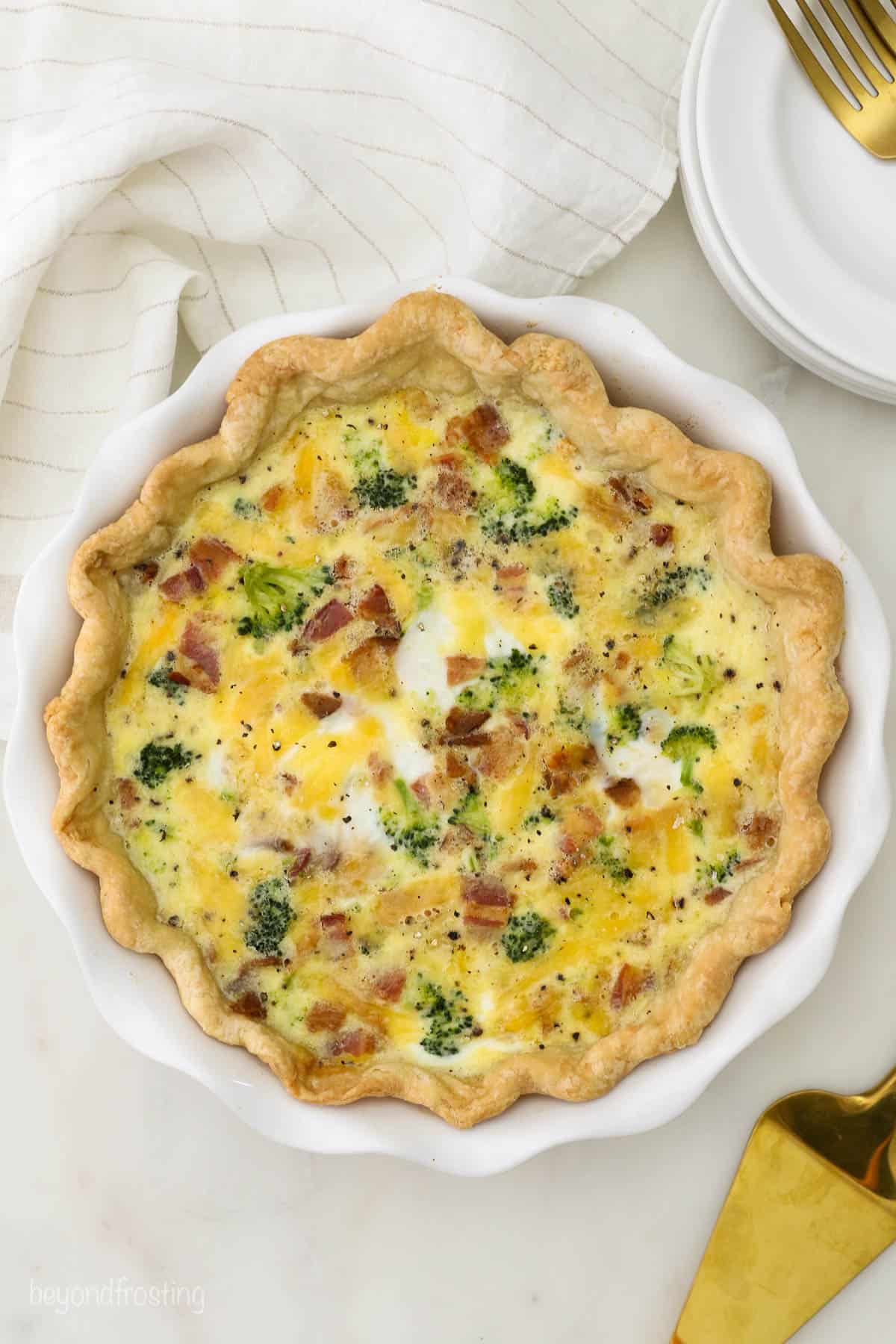 An overhead shot of a broccoli bacon quiche in a pie dish on a white countertop