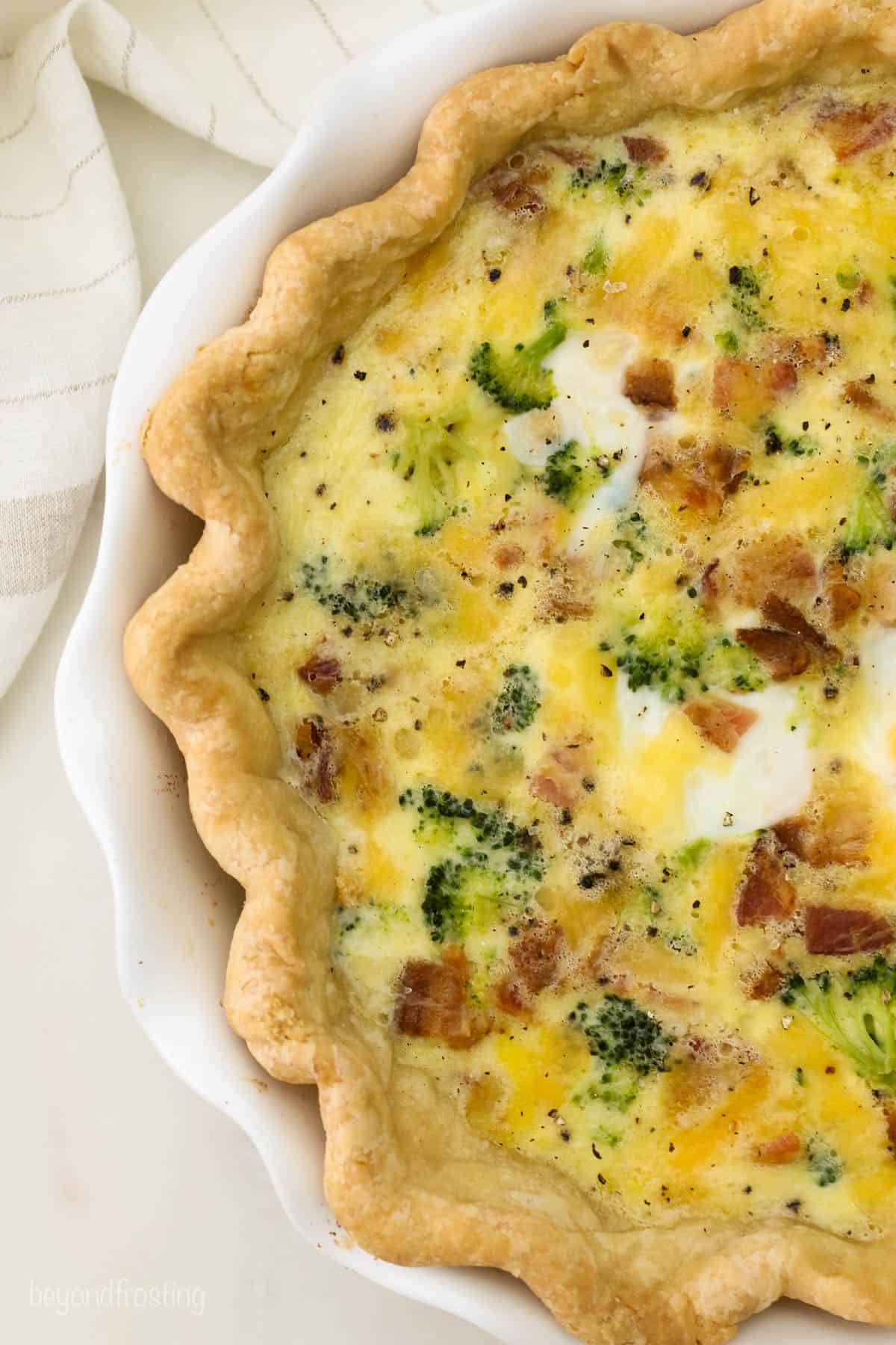 A homemade crusted quiche filled with cheese, meat and veggies in a pie plate