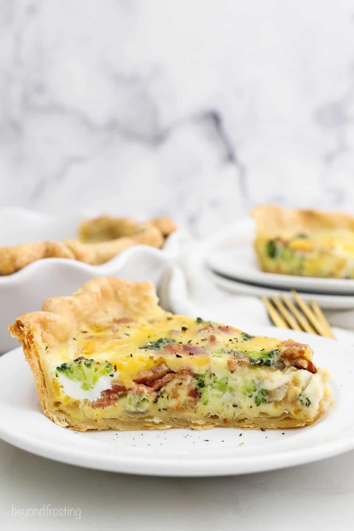 A slice of breakfast quiche on a white plate with a marble background