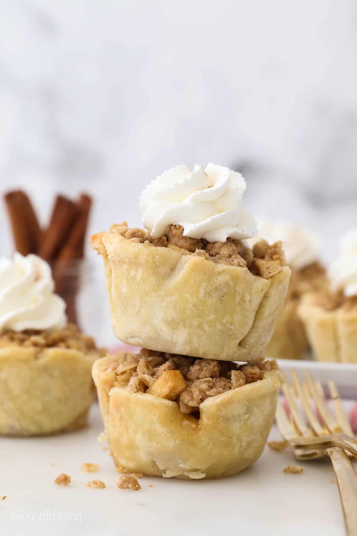 Two mini apple pies, stacked, the top one has whipped cream on top