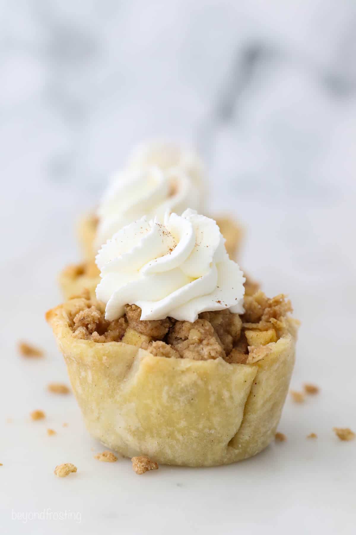 These mini apple pies are baked in a muffin tin and full of fall flavor! With gooey cinnamon apples, flaky pie crust, and a buttery crumble. Three mini apple pies lined up on a marble counter.