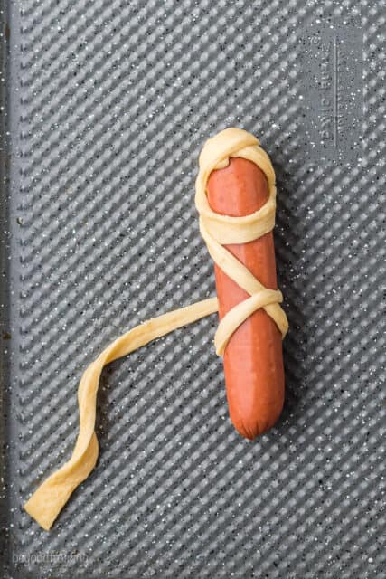 A raw hot dog being wrapped with a strip of crescent dough