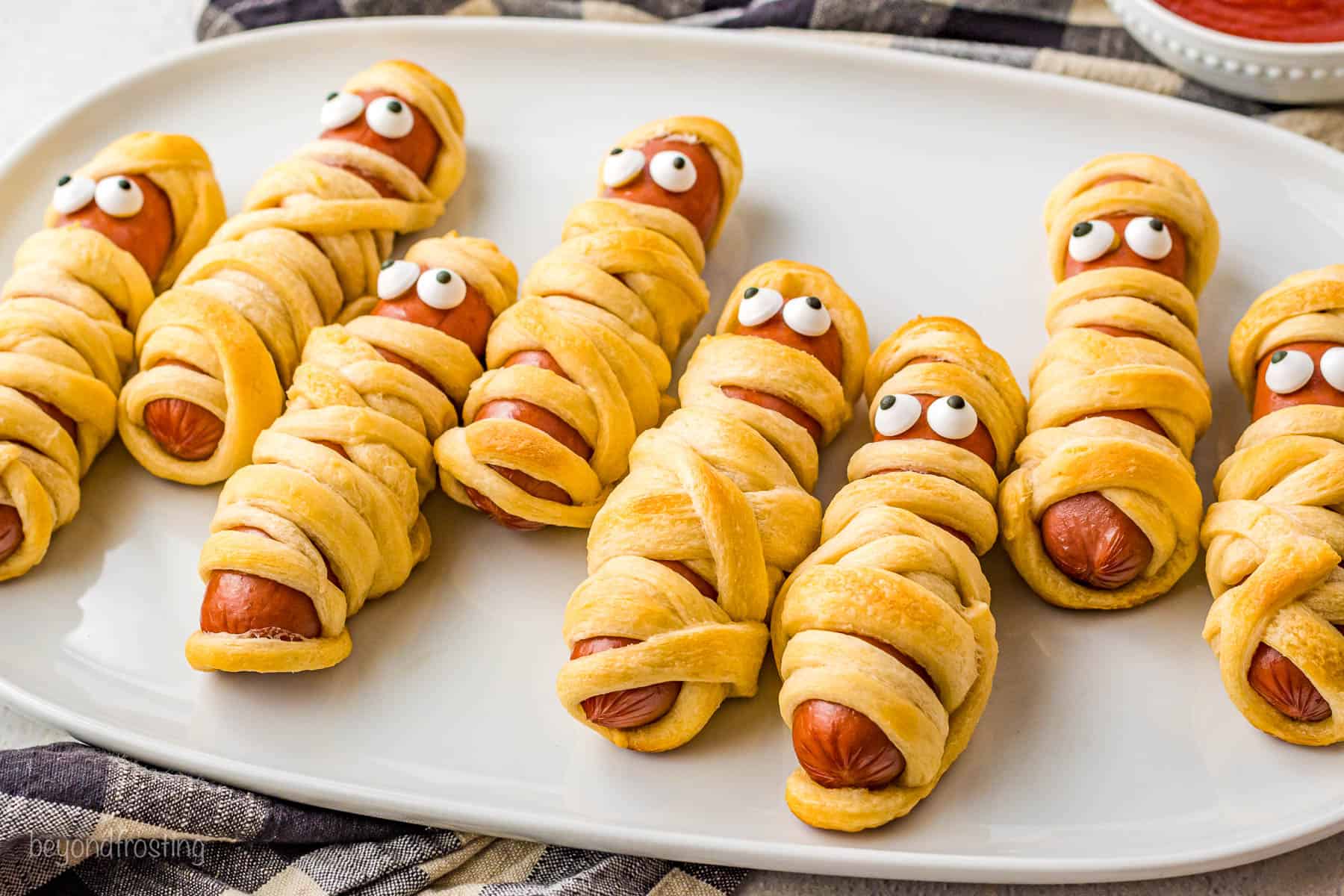 A serving platter full of crescent dough mummy hot dogs