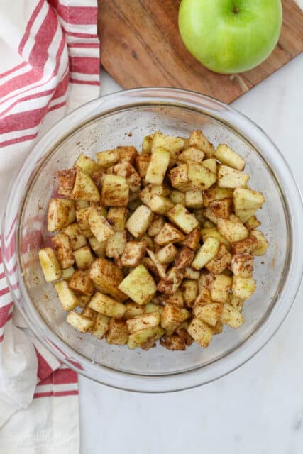 diced apples tossed with flour, sugar, and seasonings in bowl
