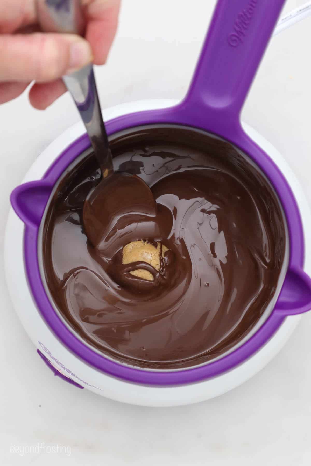 A spoon dropping a single peanut butter ball into a melting pot full of dark chocolate
