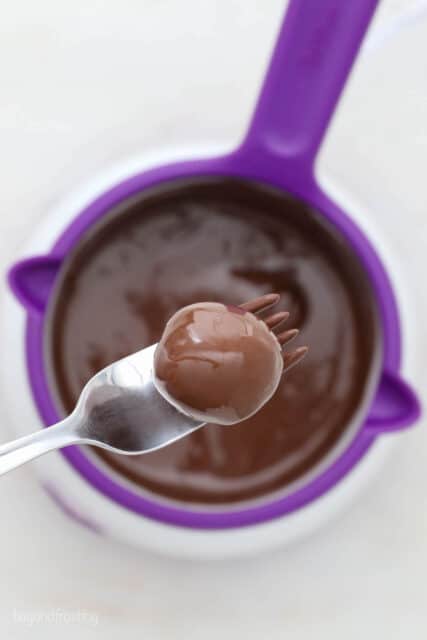 A fork lifting a dipped peanut butter ball out of a bowl of melted chocolate