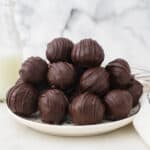 A pile of chocolate covered peanut butter balls on a plate with a raised rim