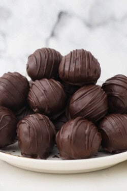 A pile of chocolate covered peanut butter balls on a plate with a raised rim